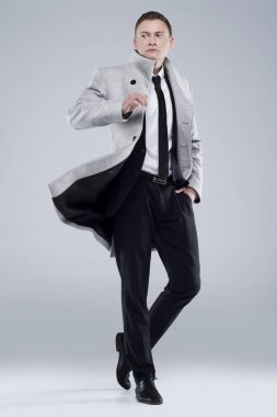 Yakışıklı genç bir gri ceket ve siyah takım elbise gri bir arka plan üzerinde duruyor