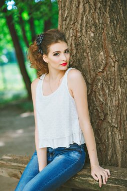 genç kadın açık havada beyaz bir t-shirt ve jeans, parlak makyaj, kırmızı dudaklı. Kameraya bakarak