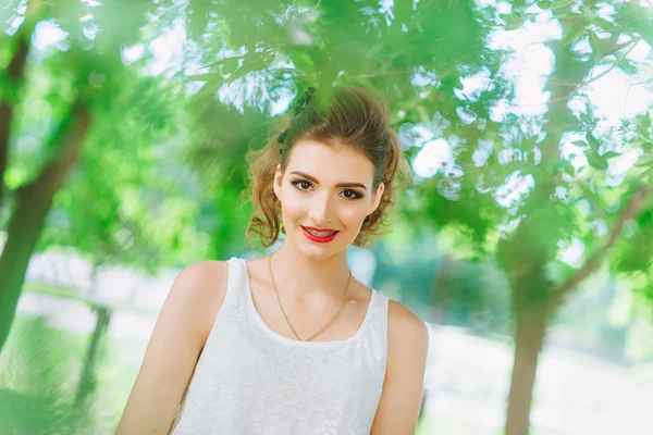 Mujer joven al aire libre en una camiseta blanca y jeans, con maquillaje brillante, labios rojos. Mirando a la cámara — Foto de Stock