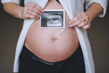 Ultrason resmini ve test şeridi ile hamile bir kadının karnı