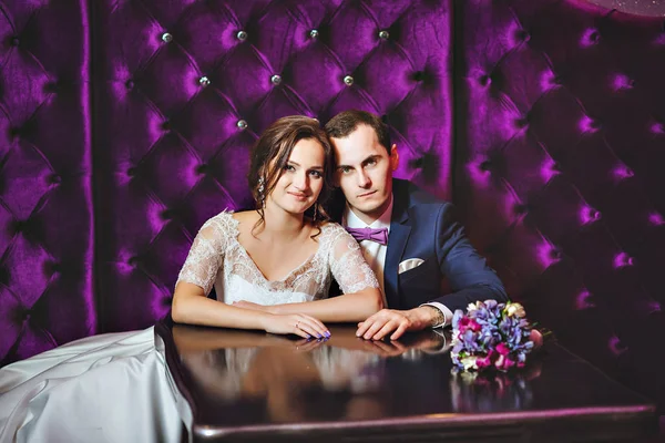 Dia do casamento. A noiva e o noivo em um interior luxuoso na cor de lavanda. Emoções de casamento. Bela noiva e elegante noivo na cerimônia . — Fotografia de Stock