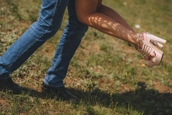Piernas pies parejas enamoradas. Él la vuelve en sus brazos, sobre la hierba verde cerca del mar . — Foto de Stock