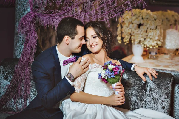 Día de la boda. Los novios en un lujoso interior en color lavanda. Emociones de boda. Hermosa novia y elegante novio en la ceremonia . — Foto de Stock