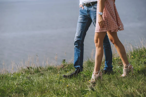 Pies piernas pareja enamorada. Caminar sobre hierba verde cerca del mar . — Foto de Stock