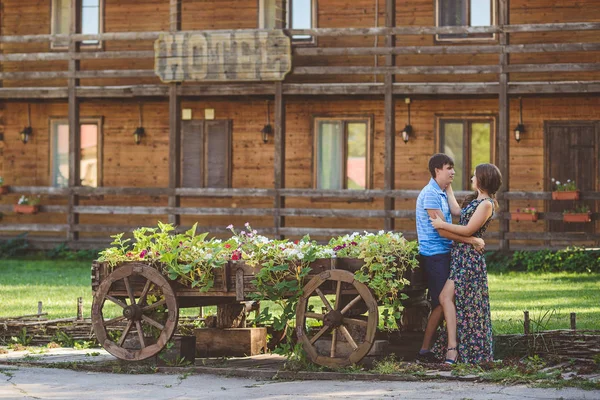 Romantikus fiatal pár átölelve egymást, közel egy dekoratív fa szekerek virággal, a háttérben a rusztikus stílus. — Stock Fotó