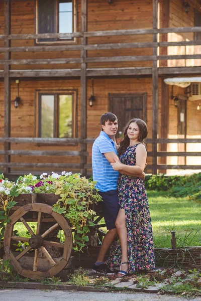 Pareja joven y romántica abrazándose entre sí cerca de un carro de madera decorativo con flores, sobre un fondo de estilo rústico . — Foto de Stock