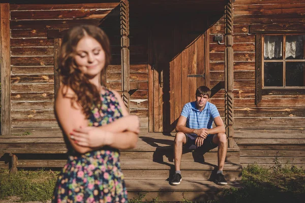 Romantikus pár, a falu közelében egy faház szeretni. Egy férfi ül a tornácon, egy fiatal nő, az előtérben. Koncepció: szerelem, romantika, nyári. — Stock Fotó