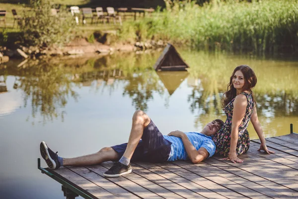 Щаслива романтична пара в селі, прогулянка по дерев'яному мосту біля озера. Чоловік на колінах молодої жінки . — стокове фото