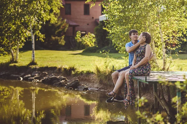 Šťastný romantický pár na dřevěném mostě nedaleko jezera. Muž opravuje mladé ženské vlasy. — Stock fotografie