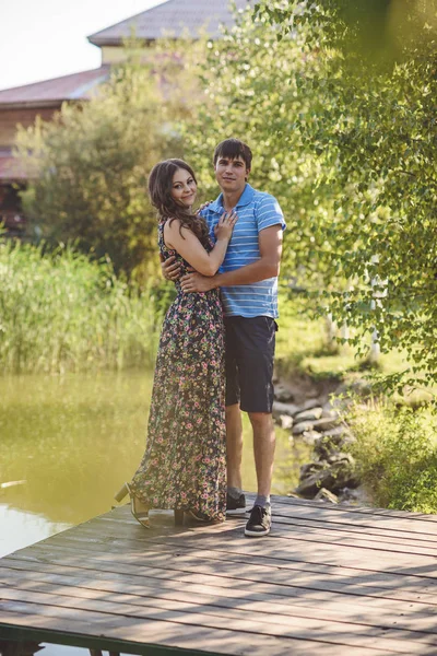 Feliz pareja romántica en un puente de madera cerca del lago. Hombre y mujer joven mirando a la cámara . — Foto de Stock