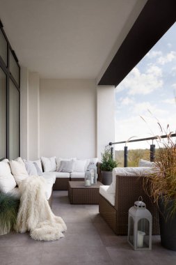 Zarif dizayn edilmiş balkon, şık rattan mobilyalar ve bir sürü rahat yastık ve battaniye.