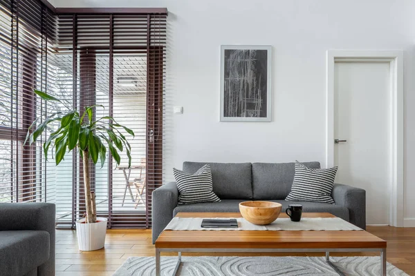 木製のブラインドと木製のコーヒーテーブルとシンプルなグレーのソファ付きのスタイリッシュなリビングルーム — ストック写真