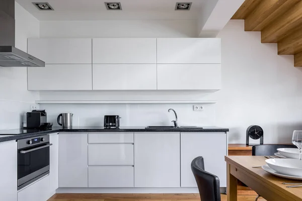 精致的厨房 白色家具 黑色台面 有木制餐桌的用餐区 — 图库照片