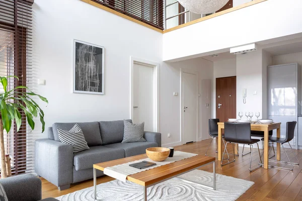 Two-floor apartment with stylish living room with grey sofa and wooden coffee table open to dining area with table for four