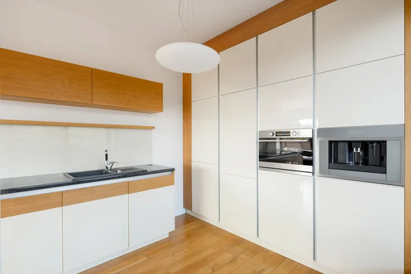 Modern white gloss kitchen with stylish wooden floor, cupboards and wall