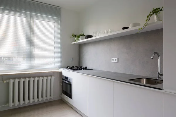 Simple kitchen with gray countertop and white furniture and vintage heater under window