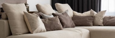 Bir sürü dekoratif yastığı ve panoraması olan bej renkli kanepe.