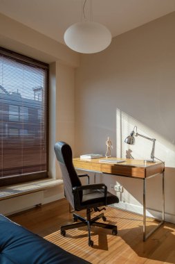 Büyük pencereli, ahşap zeminli ve küçük ahşap masalı basit bir ofis.