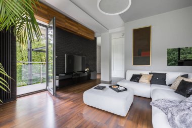 Ahşap zeminli, balkon kapısı geniş terasa açık şık bir oturma odası.