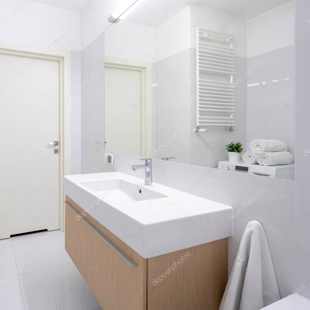Simple white bathroom with long washbasin on wooden chest with drawers