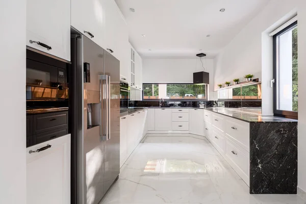 Elegant and spacious kitchen with white furniture, marble floor and big fridge