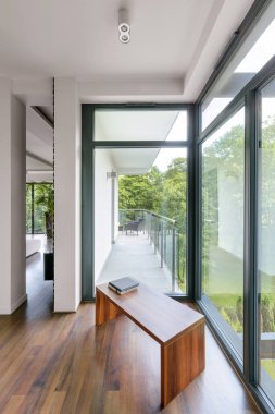 Ahşap bankı, balkon kapısı, büyük pencereleri ve terası olan zarif bir ev koridoru.
