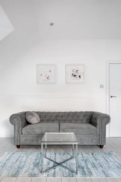 Small living room in white with gray, quilted sofa and glass coffee table