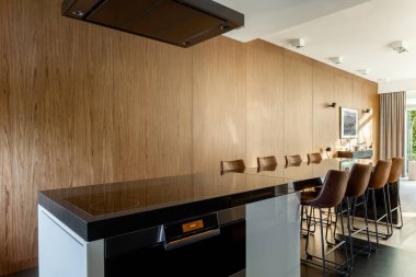 Uzun mutfak adası olan şık bir mutfak. İndüksiyon hobisi, fırın kaputu ve yemek masası var.