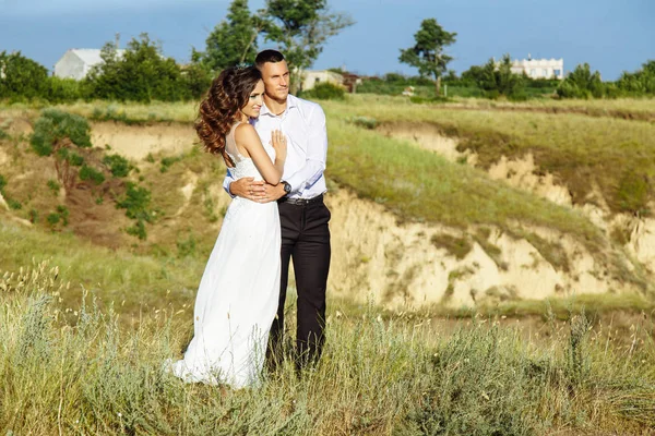 Hermosa pareja en el campo, amantes o recién casados posando en la puesta del sol con el cielo perfecto — Foto de Stock