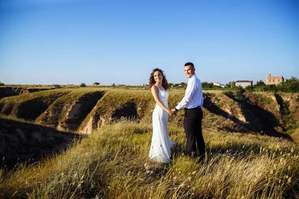 Hermosa pareja en el campo, amantes o recién casados posando en la puesta del sol con el cielo perfecto — Foto de Stock