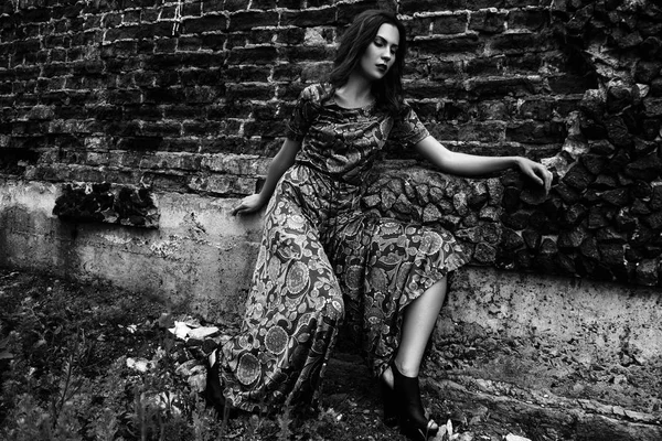 Moda ritratto all'aperto di una bella donna bruna vestita con un abito vicino al muro di mattoni. Bianco e nero — Foto Stock