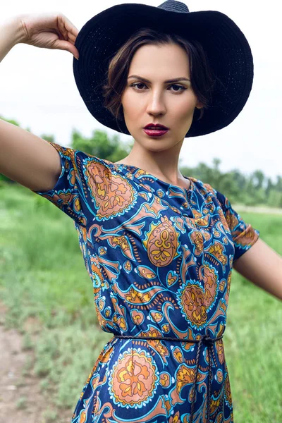 Retrato al aire libre de moda de una hermosa mujer morena vestida con un traje y un sombrero negro en el campo —  Fotos de Stock