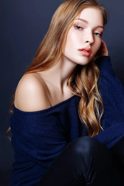 Retrato de moda de una hermosa joven con el pelo rubio. Chica en un jersey azul sobre un fondo negro —  Fotos de Stock