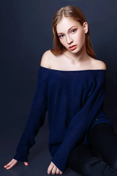 Retrato de moda de una hermosa joven con el pelo rubio. Chica en un jersey azul sobre un fondo negro — Foto de Stock