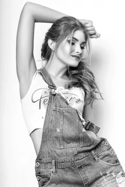 Fashion portrait of beautiful young woman with long hair. Girl in a white jersey and denim overalls on a white background. Black and white — Stock Photo, Image