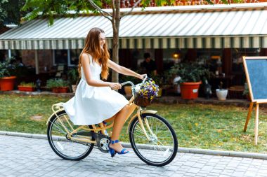 Beyaz elbiseli kız sokakta park boyunca bisiklet sürmek