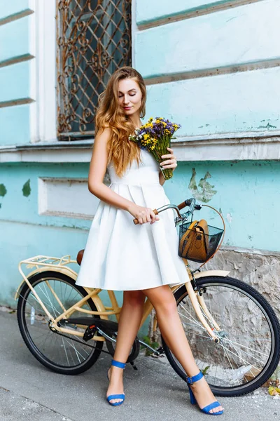 자전거와 파란색 벽 근처 꽃 흰 드레스 여자 — 스톡 사진