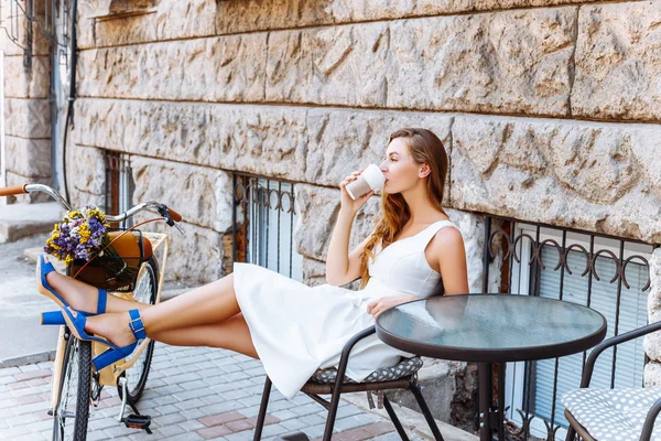 La chica está sentada en la calle con café y una bicicleta — Foto de Stock