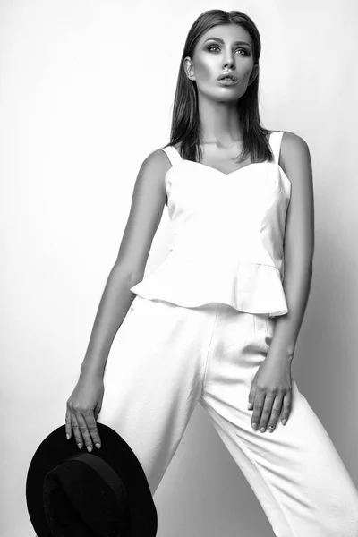 Girl in a white suit and black hat in the studio on a white background. Black and white photo — Stock Photo, Image