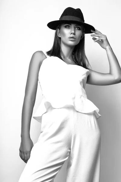 Girl in white clothes and black hat posing in studio on white background. Black and white phot — Stock Photo, Image