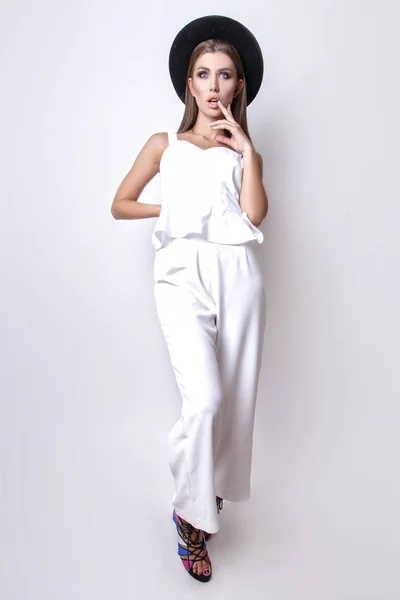 Girl in white clothes and black hat posing in studio on white background. — Stock Photo, Image