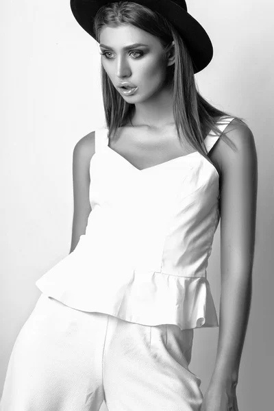 Κορίτσι σε λευκά ρούχα και μαύρο καπέλο που ποζάρουν στο studio σε λευκό φόντο. Μαύρο και άσπρο phot — Φωτογραφία Αρχείου