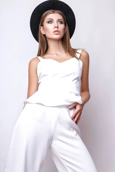 Chica en ropa blanca y sombrero negro posando en estudio sobre fondo blanco . — Foto de Stock