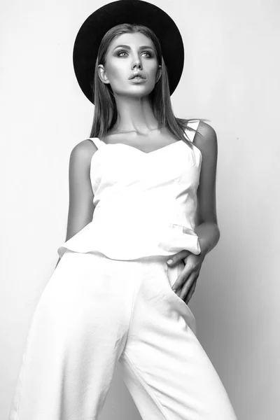 Κορίτσι σε λευκά ρούχα και μαύρο καπέλο που ποζάρουν στο studio σε λευκό φόντο. Μαύρο και άσπρο phot — Φωτογραφία Αρχείου