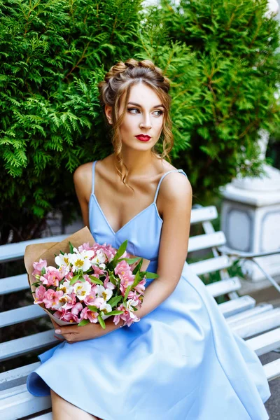 Bir buket çiçek ile bir bankta oturan genç kadın