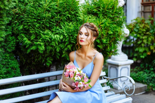 Bir buket çiçek ile bir bankta oturan genç kadın