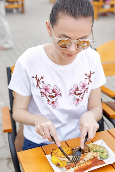 El festival de comida local. Una hermosa chica come salchichas fritas y verduras —  Fotos de Stock