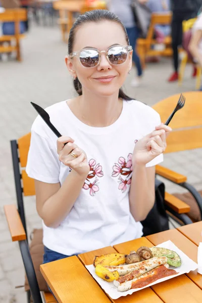 El festival de comida local. Una hermosa chica come salchichas fritas y verduras —  Fotos de Stock