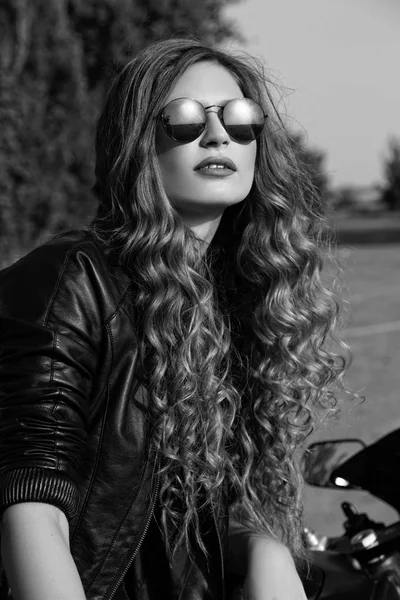 genç kadın deri giysiler ve güneş gözlüğü yakınındaki bir motosiklet. Siyah ve beyaz fotoğraf