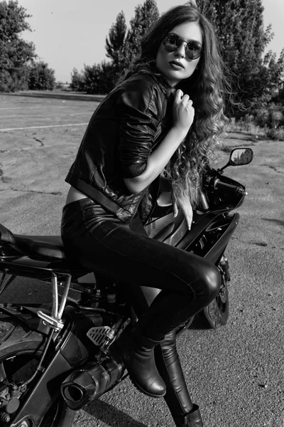 genç kadın deri giysiler ve güneş gözlüğü yakınındaki bir motosiklet. Siyah ve beyaz fotoğraf